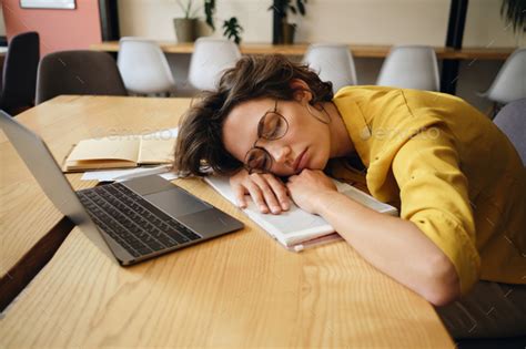 Young Tired Woman In Eyeglasses Fall Asleep On Desk With Laptop And
