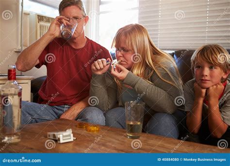 Parents Sit On Sofa With Children Taking Drugs And Drinking Stock Photo