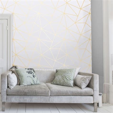 A Living Room With A White Couch And Gold Geometric Wallpaper