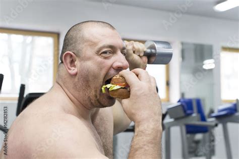 A Big Fat Hungry Man Eats A Hamburger With Meat And Cheese In The Gym