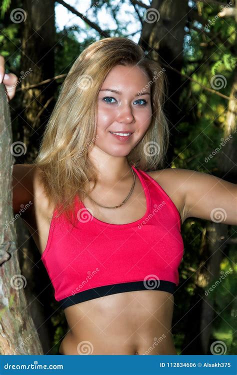 Woman In Sportswear In A Thin Pink T Shirt And Black Tight Fitting Shorts Posing In The Park In