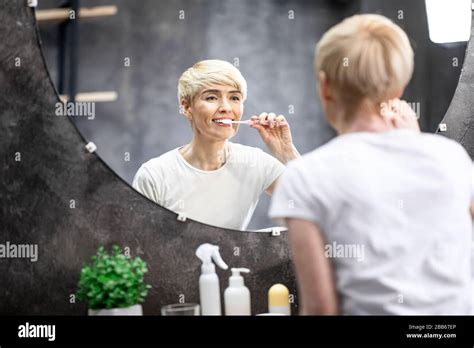 Mature Lady Brushing And Cleaning Teeth In Bathroom At Home Stock Photo