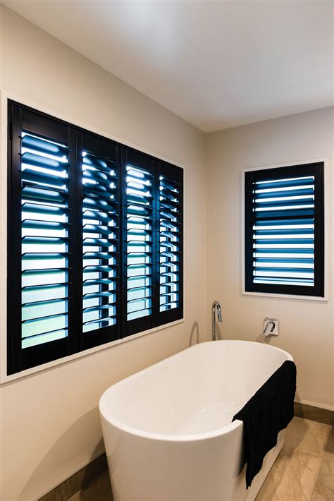 A White Bath Tub Sitting Next To Two Windows With Blinds On The Window Sill