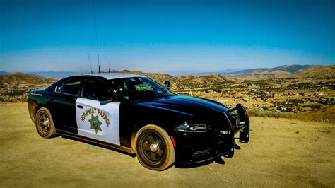 A Police Car Parked On The Side Of A Dirt Road With Mountains In The