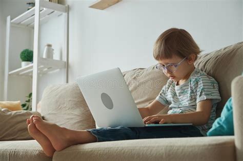 Child Using Laptop Sitting On Sofa At Home Home Schooling Distance