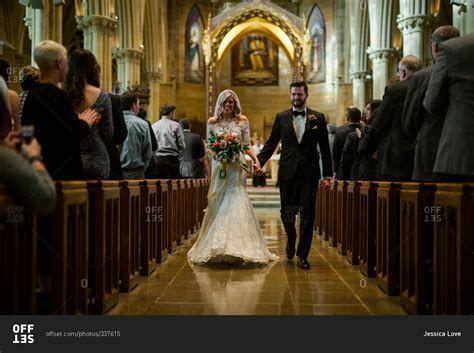 Bride And Groom Walk Down Church Aisle Holding Hands Stock Photo OFFSET