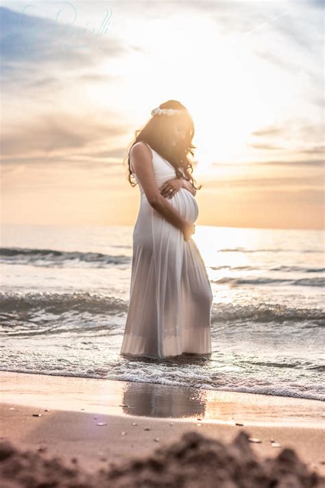 A Pregnant Woman Standing On The Beach At Sunset