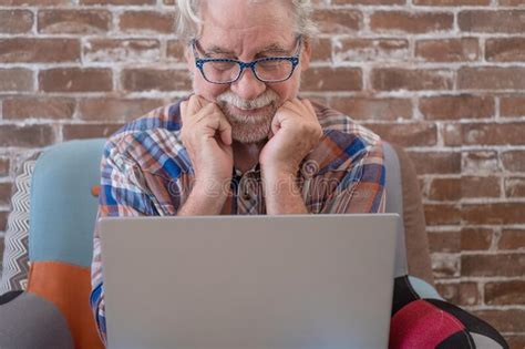 Smiling Senior Man Sitting At Home On Armchair Using Laptop Computer