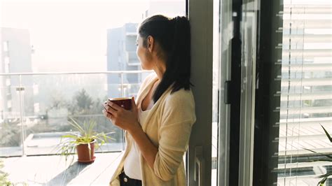 Beautiful Young Woman Relaxing On Balcony With City View Holding A Cup