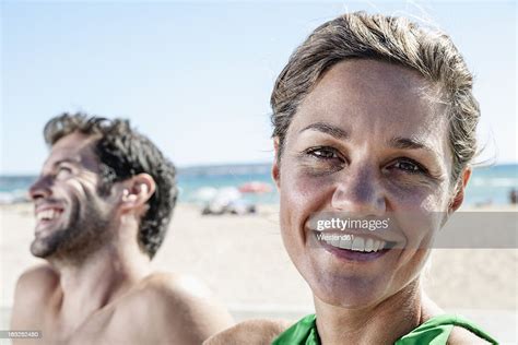 Spain Mid Adult Couple Sitting At Beach Smiling High Res Stock Photo