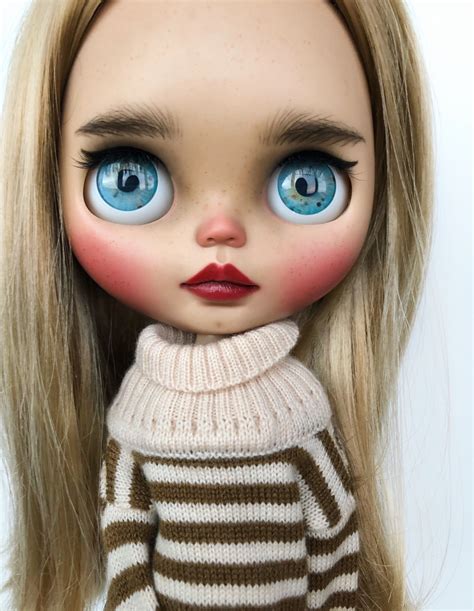 A Doll With Long Blonde Hair And Blue Eyes Wearing A Brown Striped