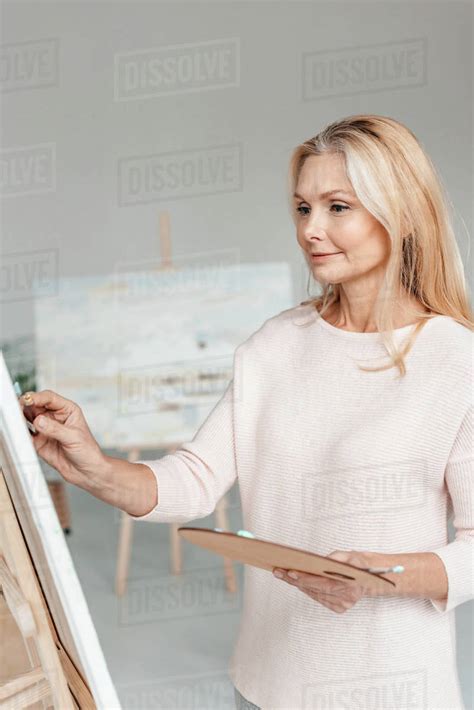 Beautiful Mature Female Artist Painting On Easel In Art Studio Stock
