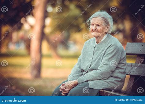 Portrait Of Senior Woman Sitting On Bench In Autumn Park Old Lady
