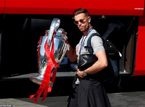 A Man Walking Past A Red Bus Holding A Silver Trophy
