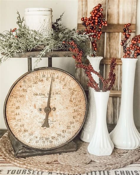 Two White Vases With Red Berries And Greenery Sit On A Table Next To An