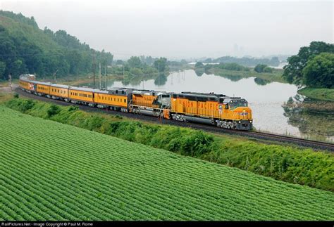 A Yellow Train Traveling Down Tracks Next To A Lush Green Field With