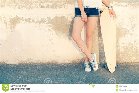 Girl Standing Near Wall With Her Legs Crossed Holding Her Longboard