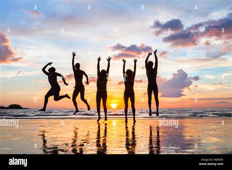 Grupo De Personas Saltando Por La Playa Al Atardecer Siluetas De Feliz