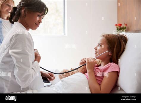 female doctor letting girl patient listen to her chest with stethoscope in hospital bed stock