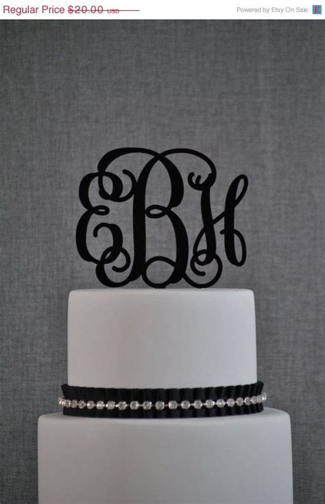 A White Cake Topped With A Black Monogrammed Topper And Two Initials On It