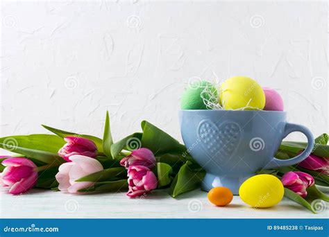 Easter Hand Painted Eggs In Blue Cup And Pink Tulips Background Stock