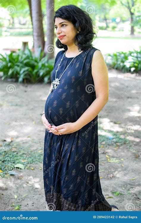 a pregnant indian lady poses for outdoor pregnancy shoot and hands on belly indian pregnant