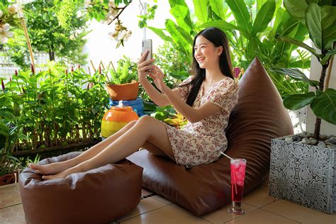 pretty asian girl relaxing on sofa bed and browsing internet on photograph by anek suwannaphoom