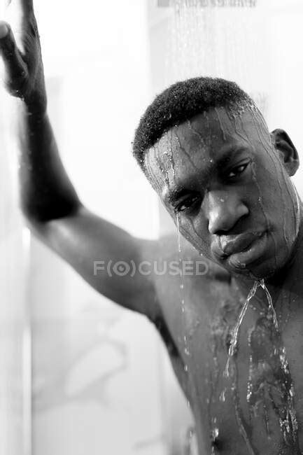 Black And White Of Emotionless Young Black Guy Taking Shower In Light