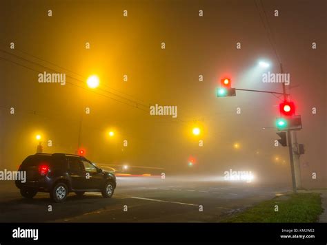 Thick Fog Over Empty Road With Lonely Car And Traffic Lights At Night