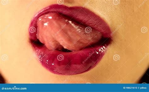 beautiful female tongue licking her lips with bright deep red plum berry glossy lipstick tint