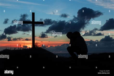 Man Kneeling By A Cross In Prayer As The Day Finishes Stock Photo Alamy