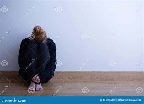 Sad Girl Sitting Curled Up On The Floor Copy Space On Empty Wall Stock