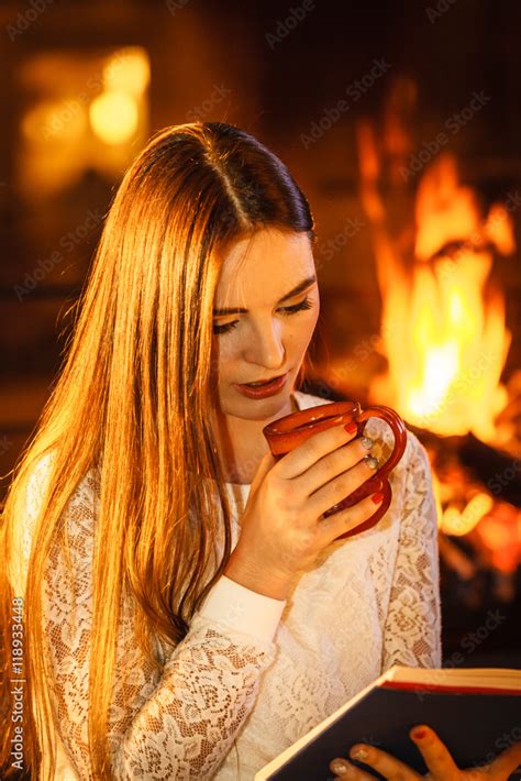 foto stock woman drinking coffee reading book at fireplace adobe stock