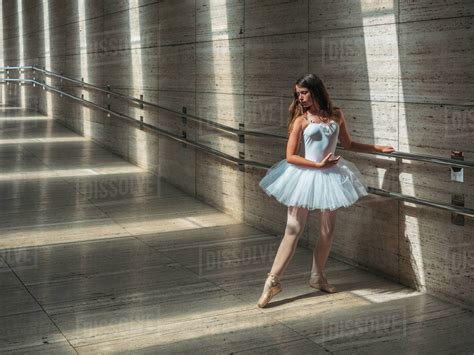 Ballerina In White Ballet Tutu Performing Exercises At Rail In Contrast