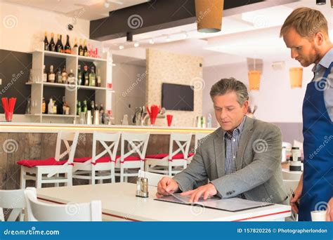 Young Waiter Taking Orders From Customer At Restaurant Stock Photo
