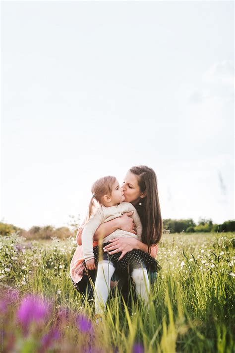 Mother Kissing Her Cute Daughter While Playing On A Summer Field By