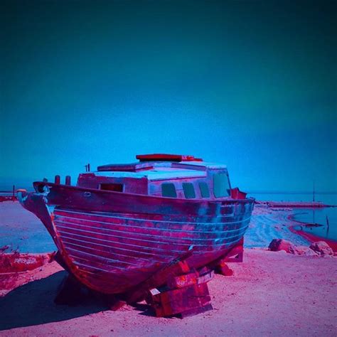 A Boat Sitting On Top Of A Sandy Beach Next To The Ocean Under A Blue Sky