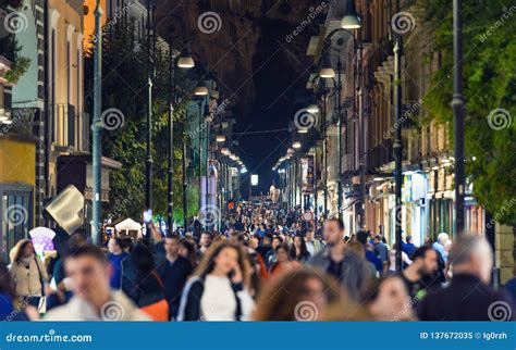 People Walk At Night Along Corso Italia Main Shopping Street Of