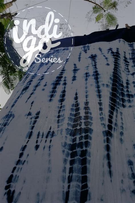 The Side Of A Building With Trees In The Background And An Indigo Blue Tie Dyed Sign That Says