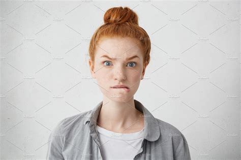 Headshot Of Anxious Redhead Freckled Caucasian Girl Raising Eyebrows And Biting Lower Lips
