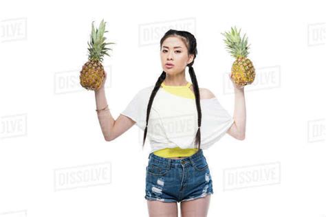 Serious Young Asian Woman Holding Ripe Pineapples And Looking At Camera Isolated On White