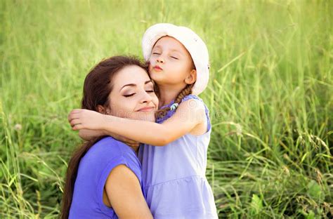Beautiful Mother Hugging And Kissing Her Cute Small Daughter On Summer Green Grass Background