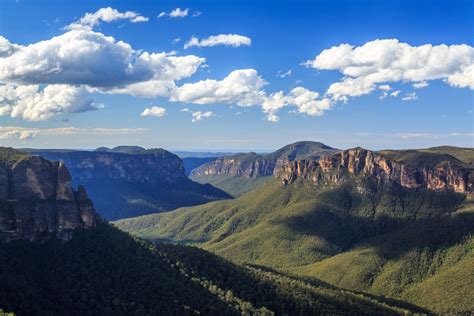 The Blue Mountains Are Surrounded By Lush Green Trees And Clouds In The