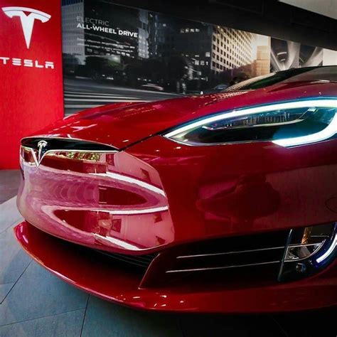 The Front End Of A Red Tesla Car In A Showroom With Its Lights On
