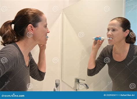 Woman Brushing Teeth With Electric Toothbrush Looking At Mirror