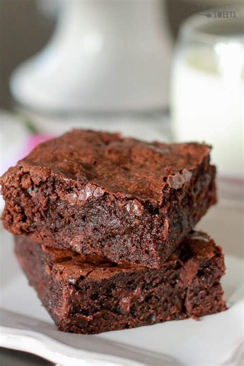 Two Brownies Stacked On Top Of Each Other On A Plate Next To A Glass Of