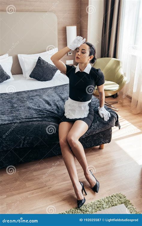 Maid In White Gloves Sitting On Bed And Touching Forehead With Closed Eyes Stock Image Image