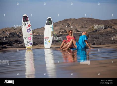 Two Blonde Girls On The Beach Laughing And Having Fun With Their Surfboard After Surfing Stock