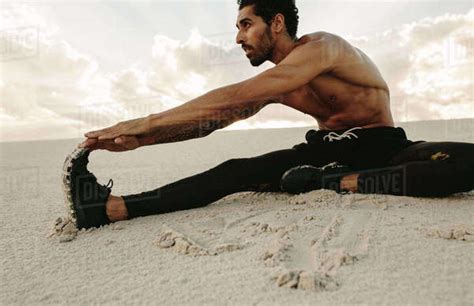 Athlete Doing Stretching Workout Sitting On Sand Dune Runner Sitting