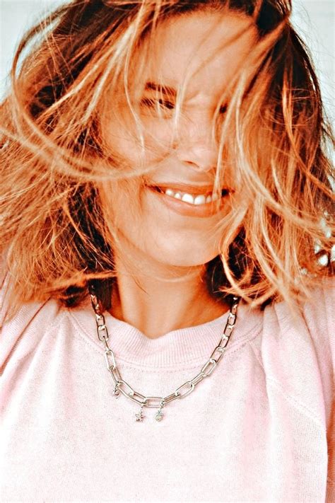 a woman with blonde hair smiling and wearing a pink shirt silver chain necklace on her neck